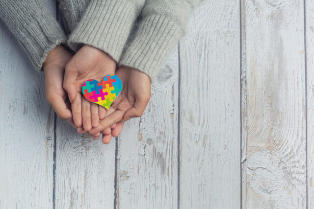 Vacuna covid y autismo: adulto y niño sosteniendo un corazón con los característicos colores del autismo.