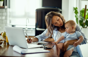 Returning to Work After Childbirth: A Physical and Emotional Challenge New Mothers Must Be Prepared For/Regresar al trabajo tras el parto: un reto físico y emocional que las nuevas madres deben afrontar preparadas Young working mother planning home budget while being with her baby at home.