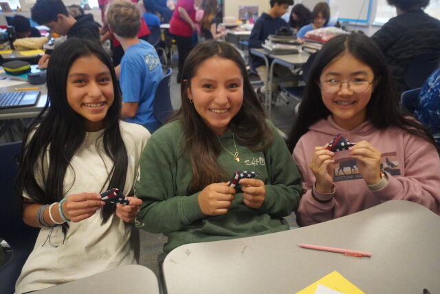Flag 2: Sussex Academy students (l-r) Sofia Morales-Chaj, Luciany Perez-Perez, and Anna Liang create pocket flags for deployed and deploying U.S. troops.